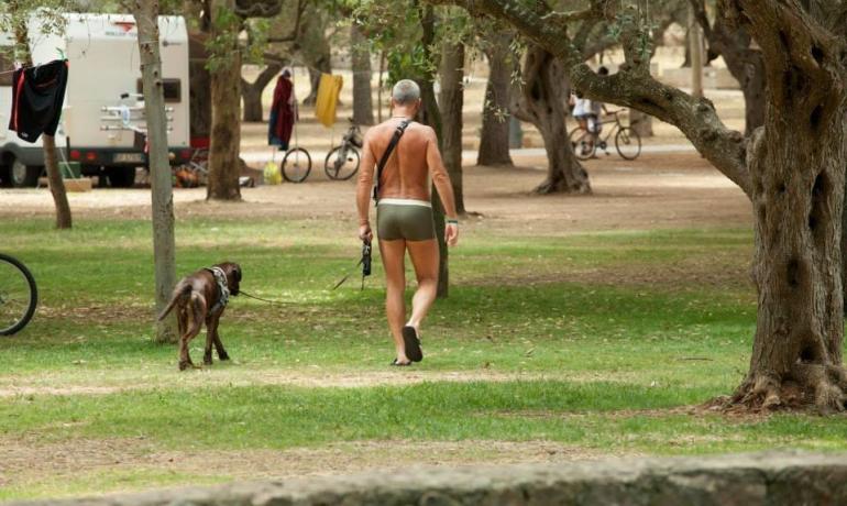 Mann in Badehose spaziert mit Hund im Park.