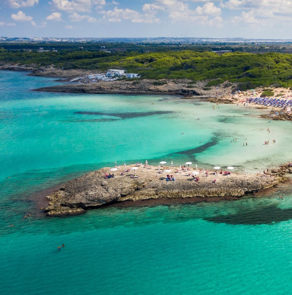 Beach with crystal-clear sea and rocks, umbrellas and swimmers.