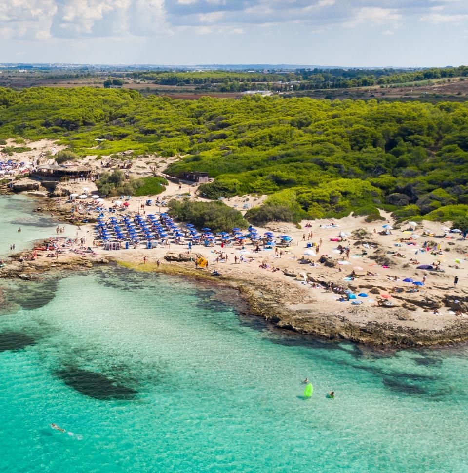 Crowded beach with blue umbrellas and crystal-clear sea.